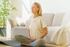 older woman sitting in her living room on a yoga mat, practicing deep breathing exercises