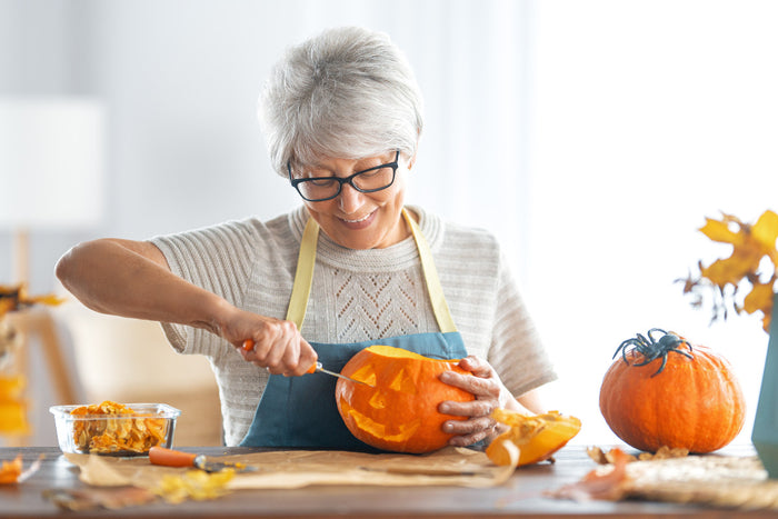 senior woman smiling as she carves a pumpkin.