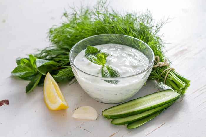 Cucumber and Mint Yogurt Dip in a glass bowl surrounded by mint leaves, cucumber slices, and a single lemon slice.