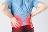 sciatica pain. image of rear view of someone holding their lower back in pain.