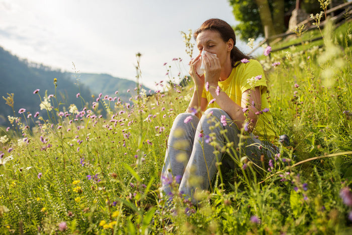 Older woman sitting in a field of flowers, blowing her nose.