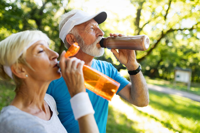 two active seniors standing outside drinking out of water bottles.