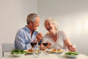older couple sitting at a table, laughing and smiling while eating pasta, salad, and drinking wine