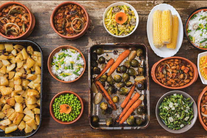 top view of various healthy Thanksgiving side dishes, including peas, roasted brussel sprouts and carrots, corn on the cob, roasted potatoes, etc.