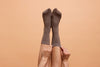 Woman sticking up her legs as she puts on long brown socks.