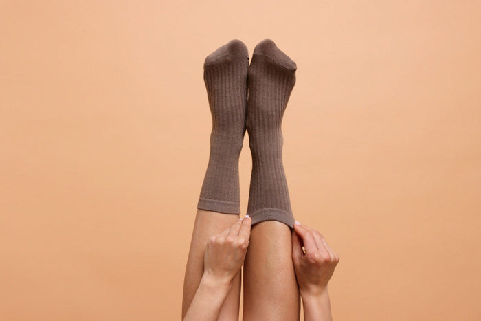 Woman sticking up her legs as she puts on long brown socks.