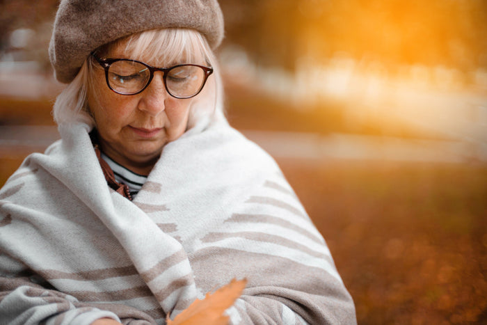 senior woman resting on a bench with a blanket in autumn.