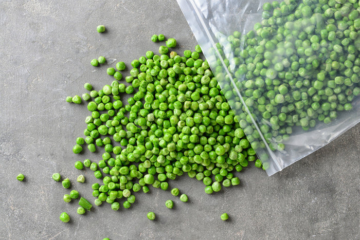Frozen bag of peas spilling out onto a concrete counter.