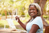 older woman smiling at the camera while painting on a canvas outside